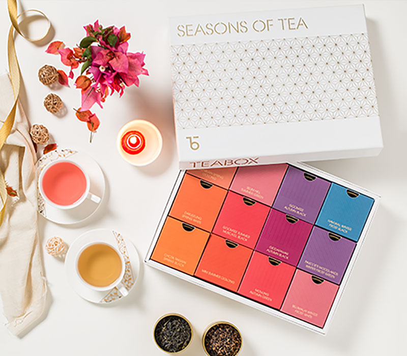 Tea gift box with twelve colorful compartments, two tea cups, a flower, and a candle.