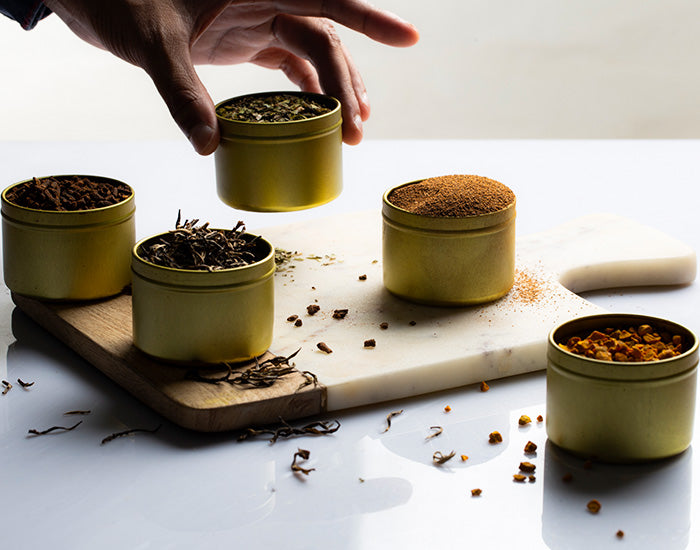 Hand selecting a spice tin from a variety on a cutting board.